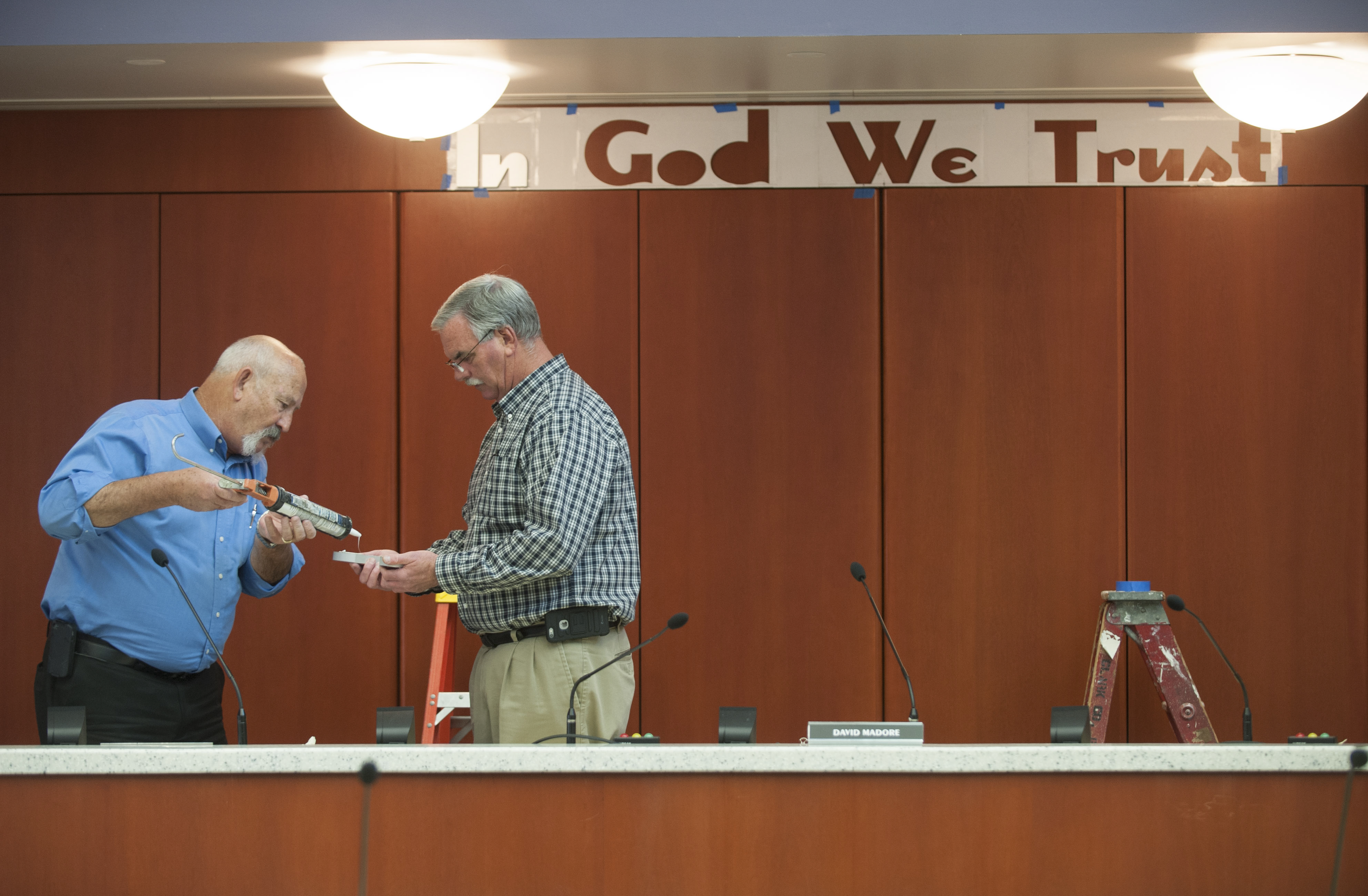 County facilities managers Darrel Stump, left and Mike Wright put glue on the back of a letter as the "In God We Trust " slogan is installed Thursday. (Natalie Behring/The Columbian)